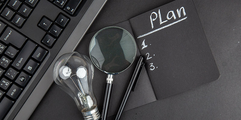 Un clavier d'ordinateur, une ampule, une loupe et un carnet avec écrit "plan"